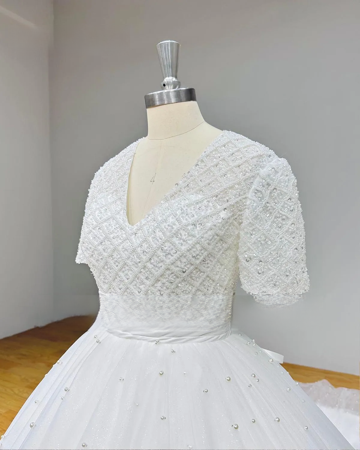 Majestic white V-neck bridal ball gown with short sleeves and a voluminous pearl-encrusted tulle skirt in a luxury wedding boutique setting.