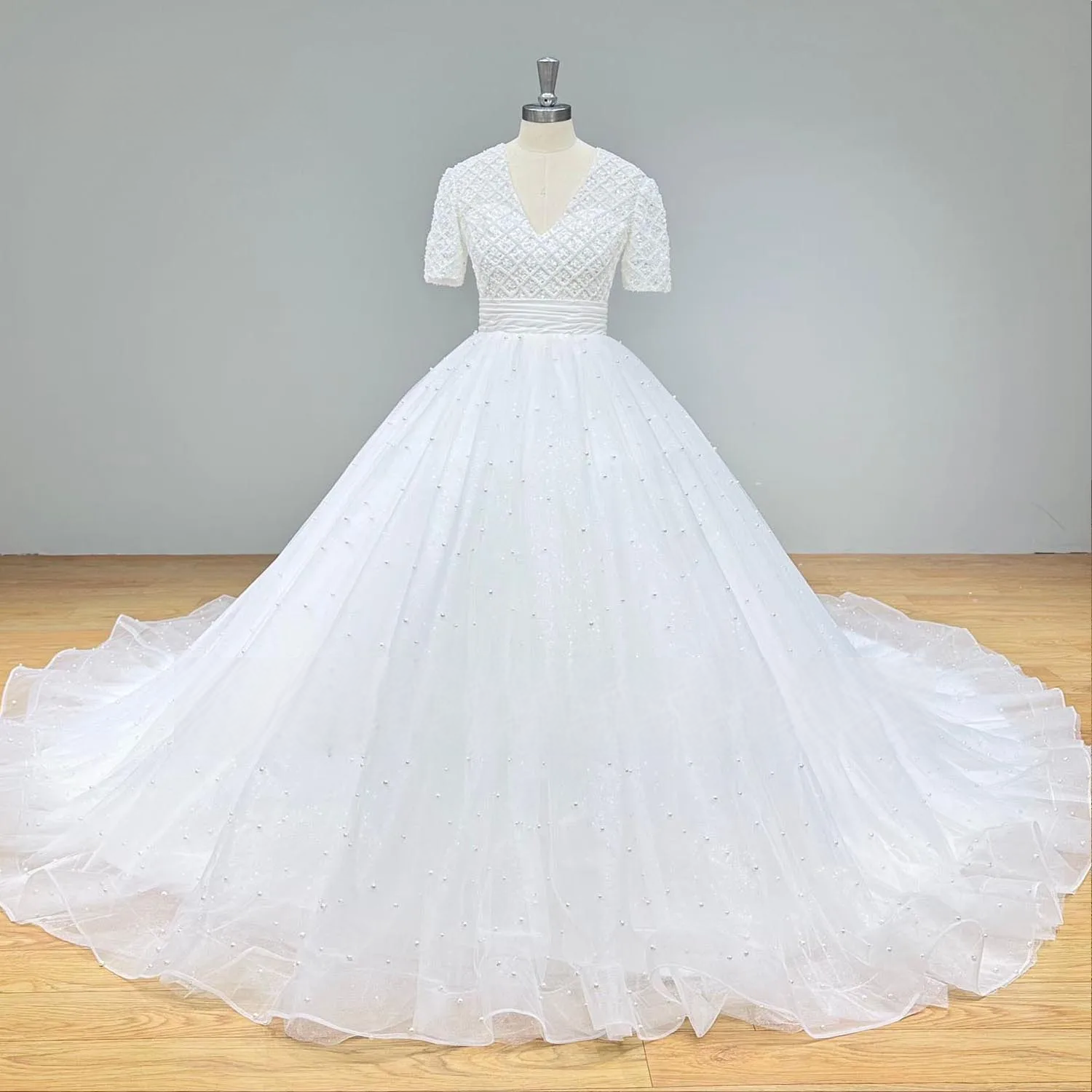 Side profile of a beaded short-sleeve wedding dress bodice with a pleated satin waistline and shimmering pearl accents.