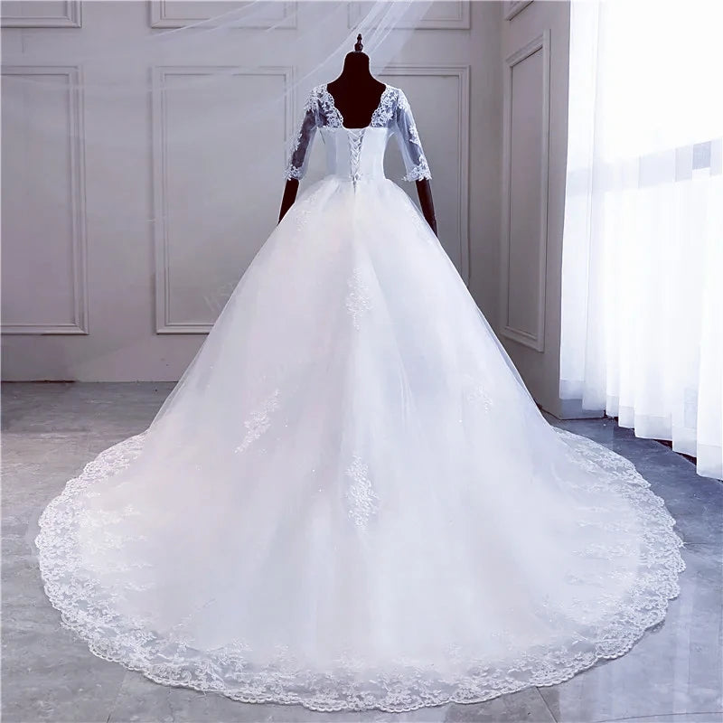 Back profile of a bridal dress on a mannequin, focusing on the lace-up corset closure, sheer lace sleeves, and a sweeping train.