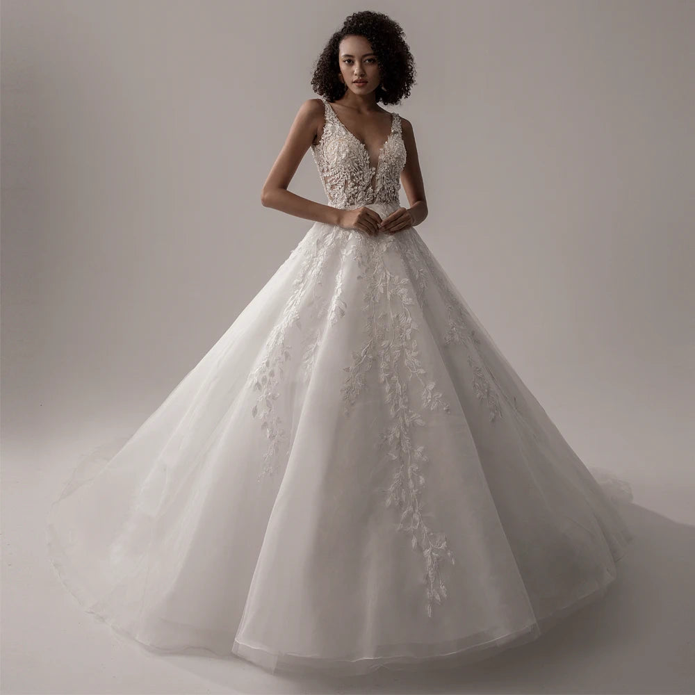 A model wearing an ivory, sleeveless, V-neck A-line wedding dress with intricate lace appliques, standing in a studio.