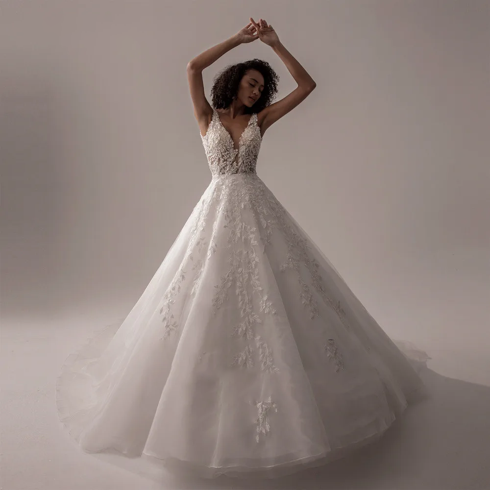 A model posing with raised arms in a sleeveless ivory lace A-line bridal gown.