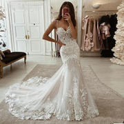 A bride wearing a vintage-style ivory mermaid wedding dress with intricate lace appliqués and an elegant court train, posing in a bridal salon.