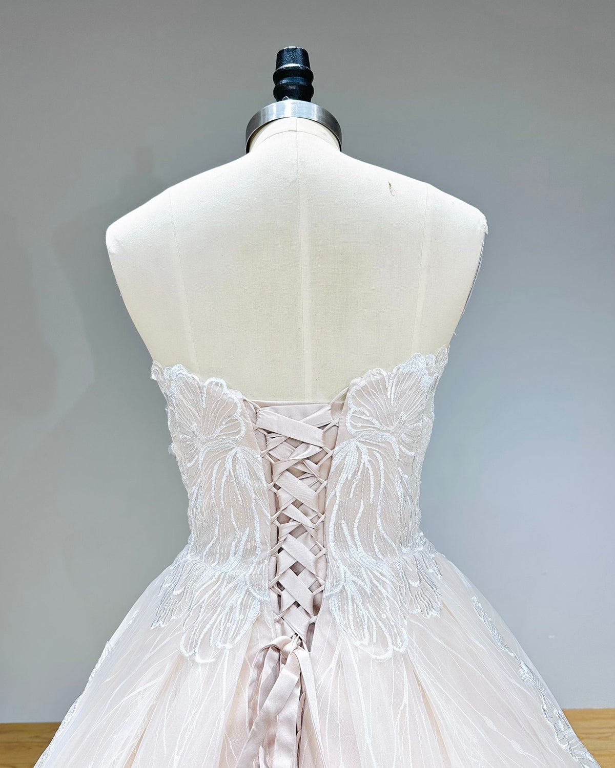 Close-up of the back of a bridal dress showcasing a satin ribbon lace-up corset closure integrated into a beautifully embroidered sweetheart bodice.