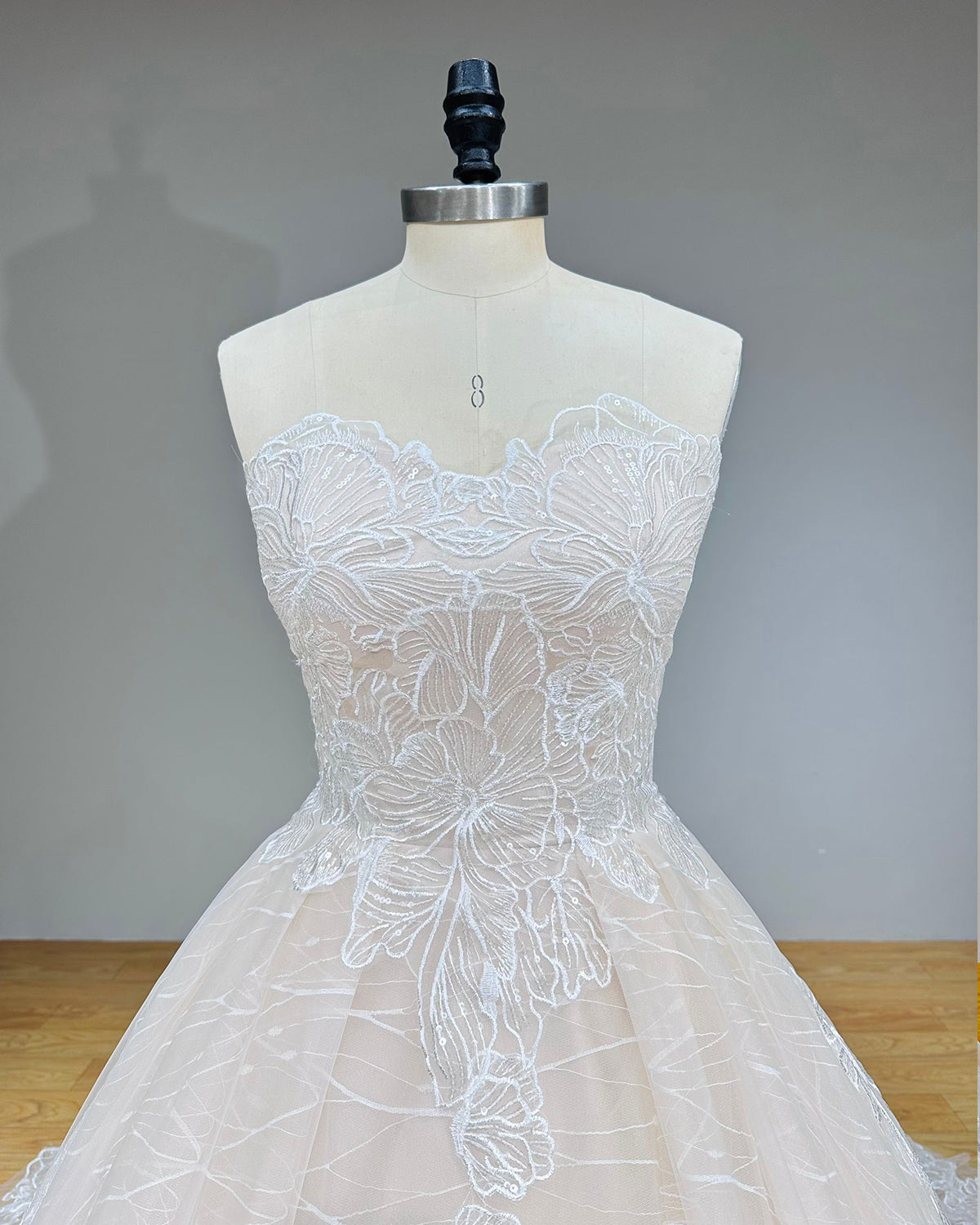 Detailed front view of a strapless sweetheart bridal bodice emphasizing the contoured scalloped edge, translucent lining, and reflective sequin appliques.