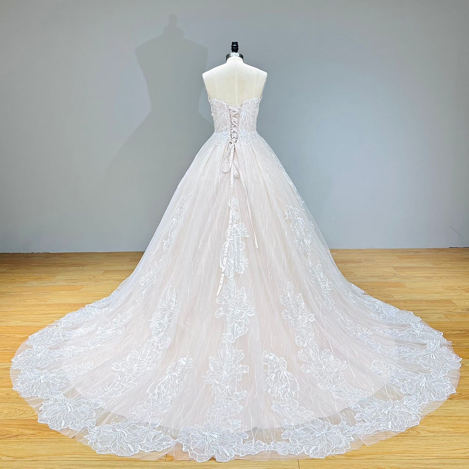 Full back view of a sweetheart lace ball gown wedding dress highlighting an adjustable corset closure and a wide, flowing train bordered with sequined appliques.