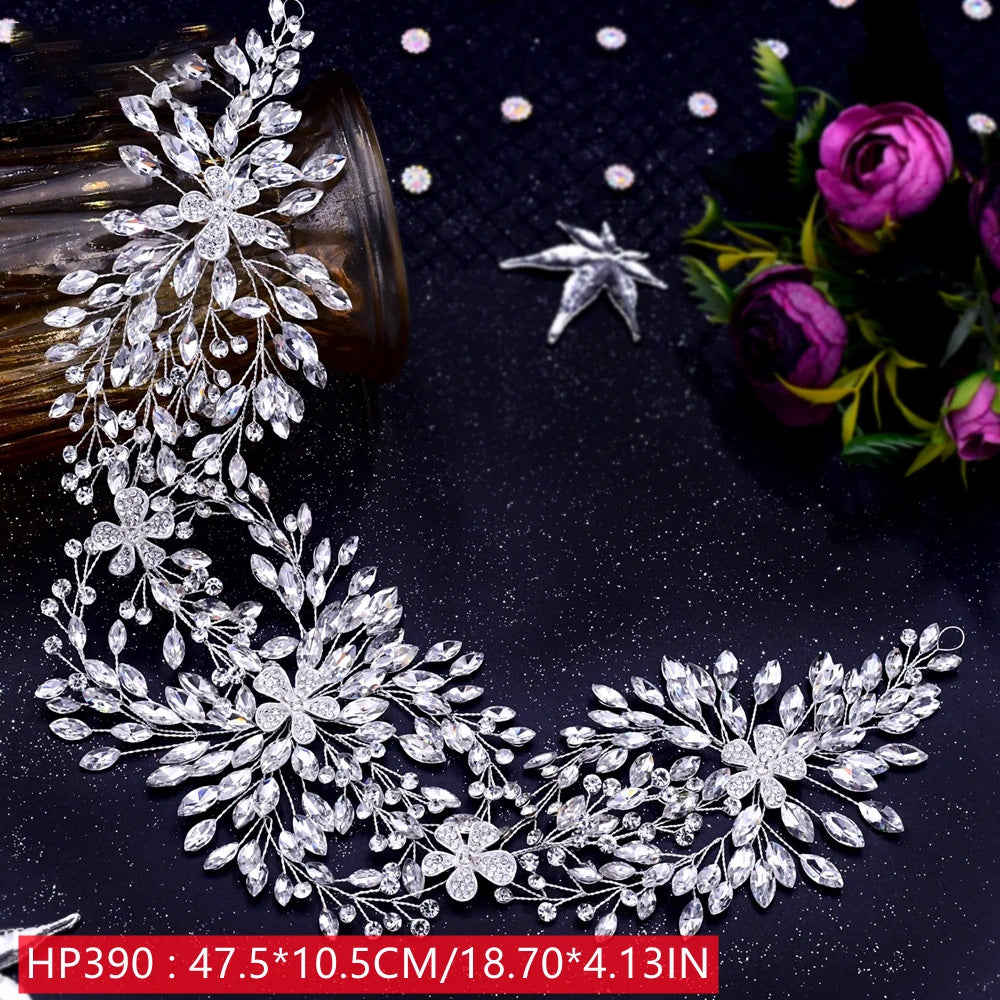 Top-down view of an intricate silver rhinestone bridal headpiece showing fine wire leaf work and clear crystal accents next to decorative purple flowers.
