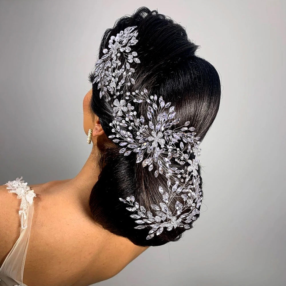 Side view portrait of a bride highlighting a multi-layered silver crystal wedding hair accessory pinned as a dramatic side spray across her dark updo hairstyle.