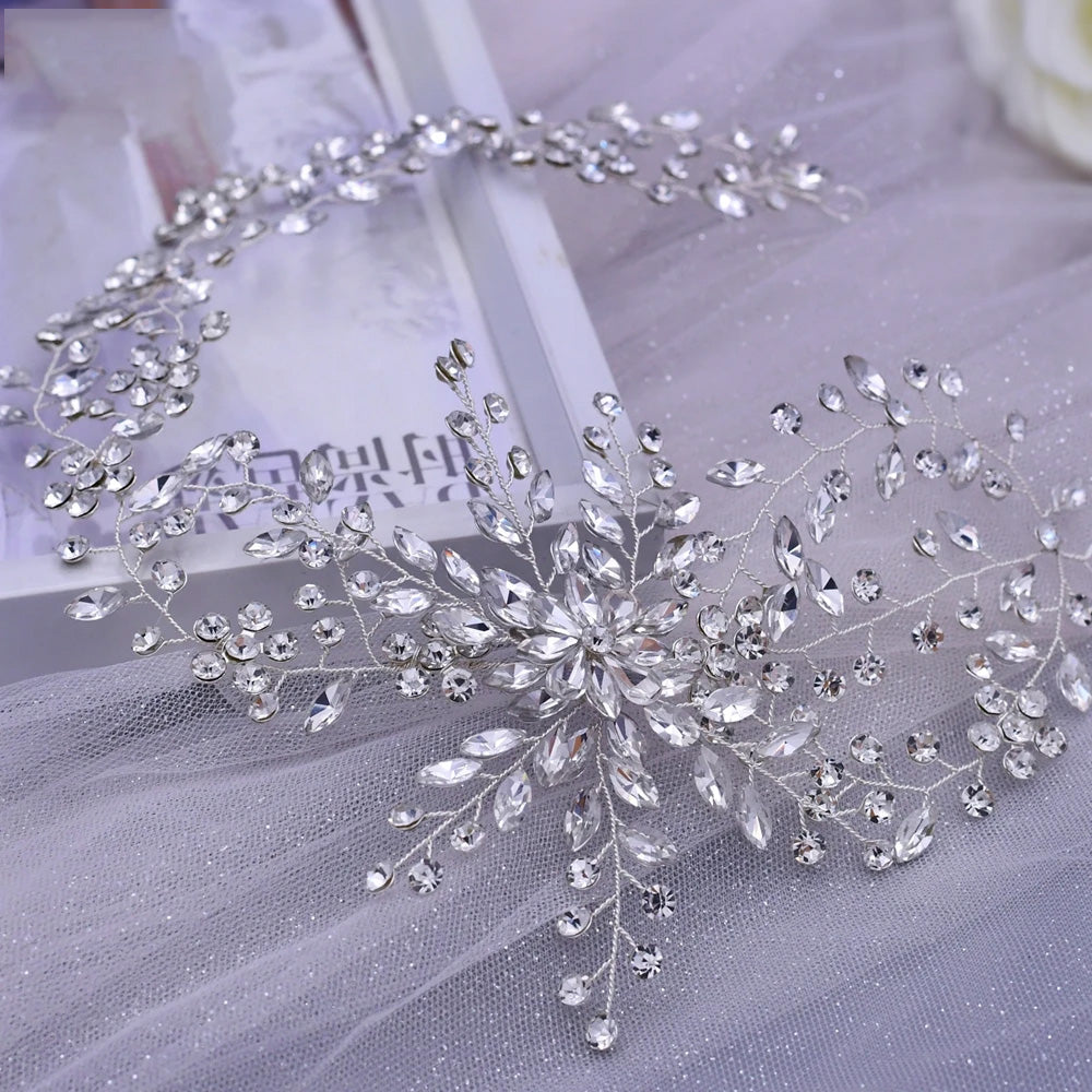 Overhead flat lay view of a wide silver crystal bridal hair piece with dense, sprawling rhinestone branches arranged elegantly over a soft white tulle fabric background.