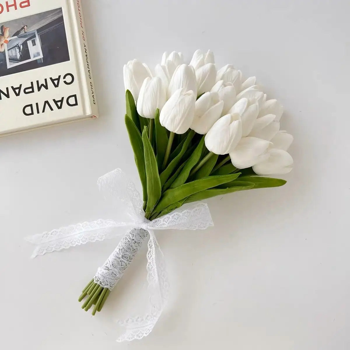 Handmade artificial bridal bouquet made of white tulips with a decorative lace-wrapped stem and ribbon.