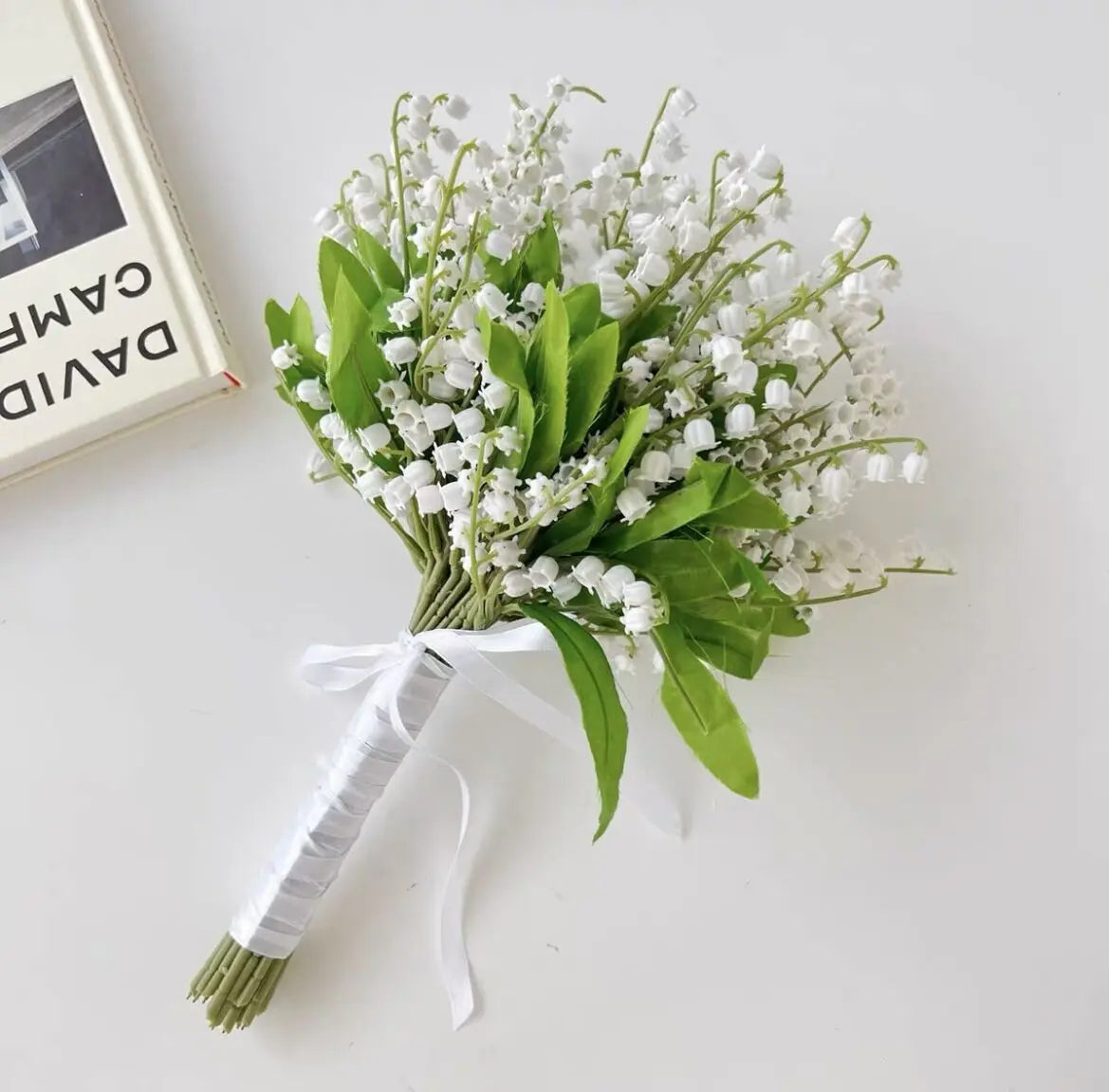 Handmade artificial wedding bouquet consisting of white lily of the valley flowers tied with a white silk ribbon.