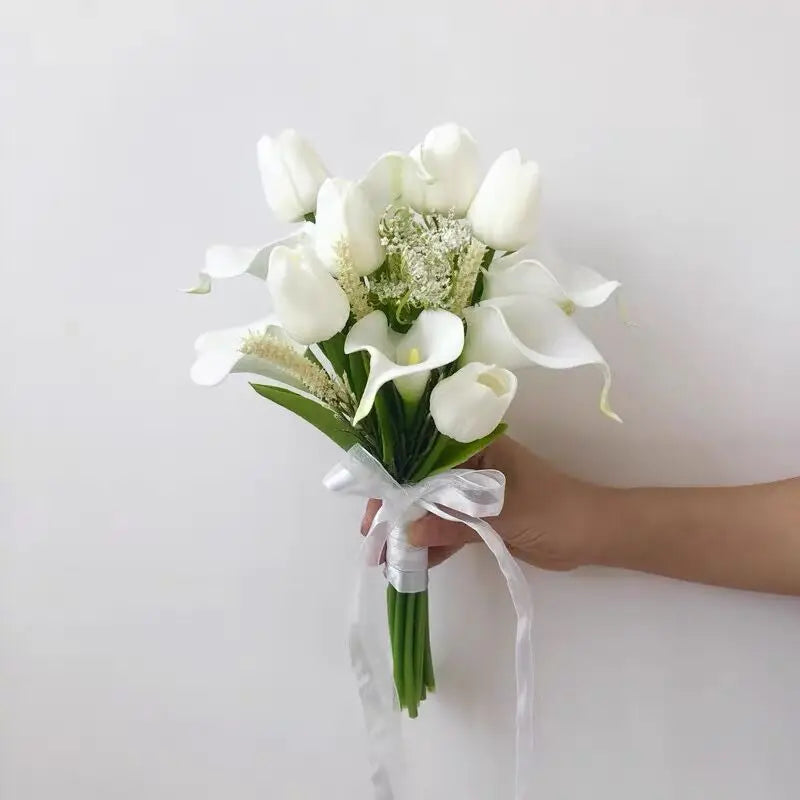Handmade artificial wedding bouquet combining white tulips and white calla lilies, held by hand with a white ribbon.