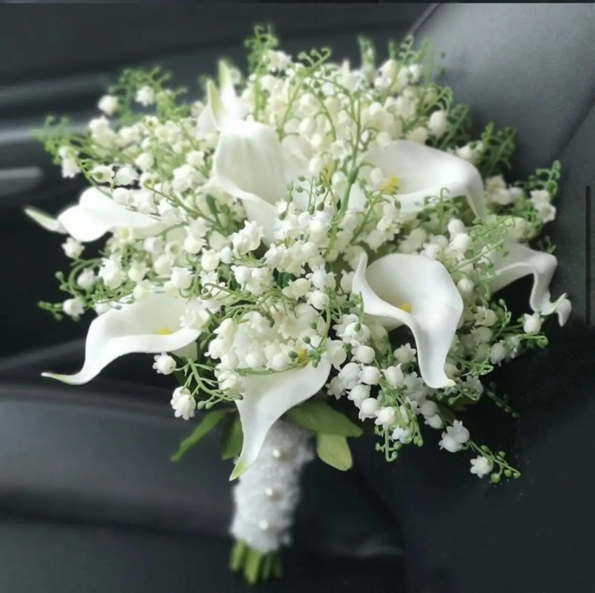 Close-up of a handmade artificial bridal bouquet with white calla lilies, lily of the valley, and a lace handle.