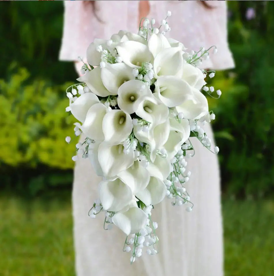 A cascading handmade artificial wedding bouquet of white calla lilies and lily of the valley held by a bride.