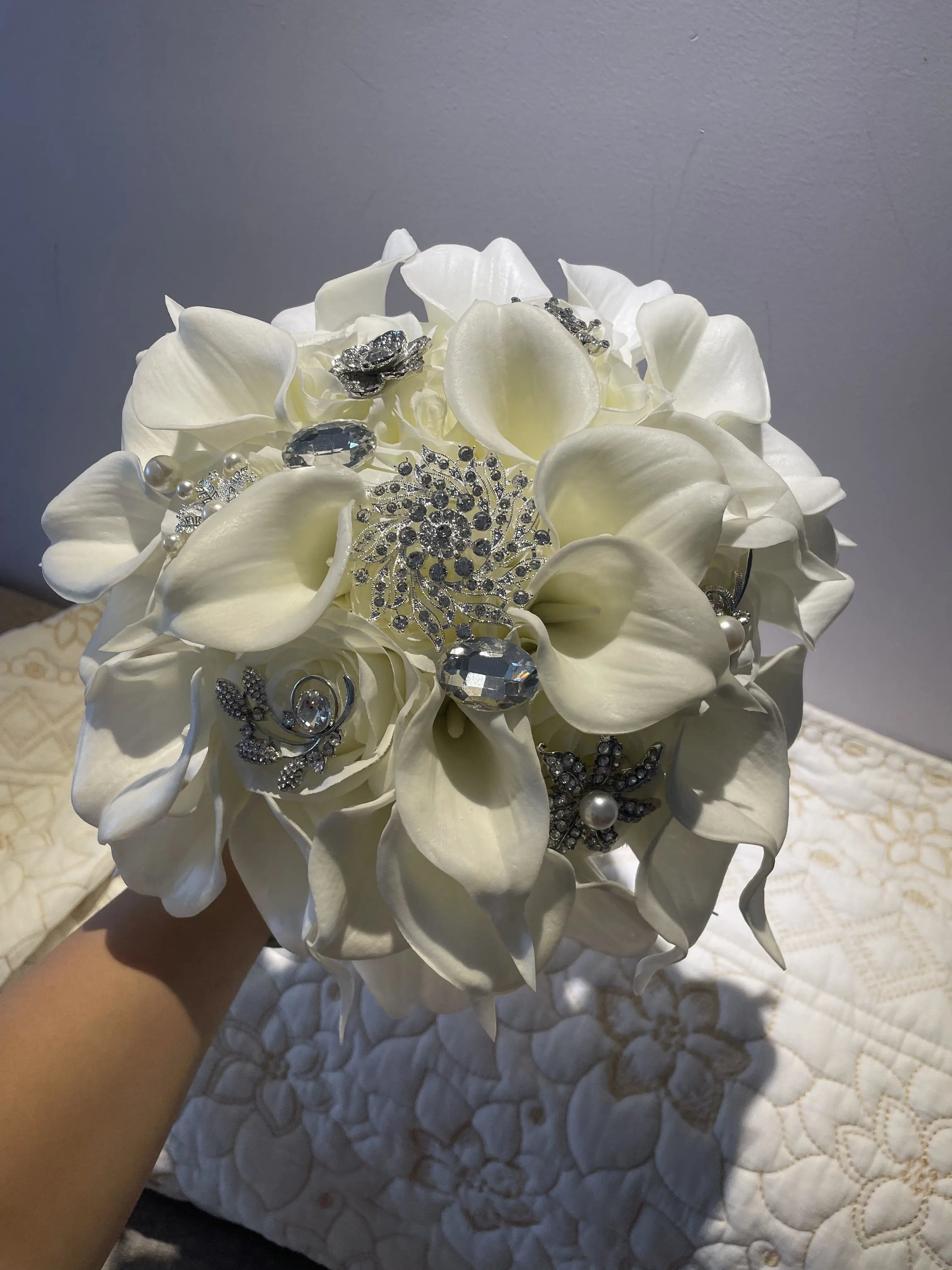 A luxury handmade bridal bouquet featuring white calla lilies decorated with intricate silver-tone rhinestone brooches.