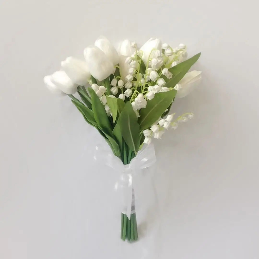 A minimalist handmade artificial wedding bouquet of white tulips and white lily of the valley with a simple white ribbon.