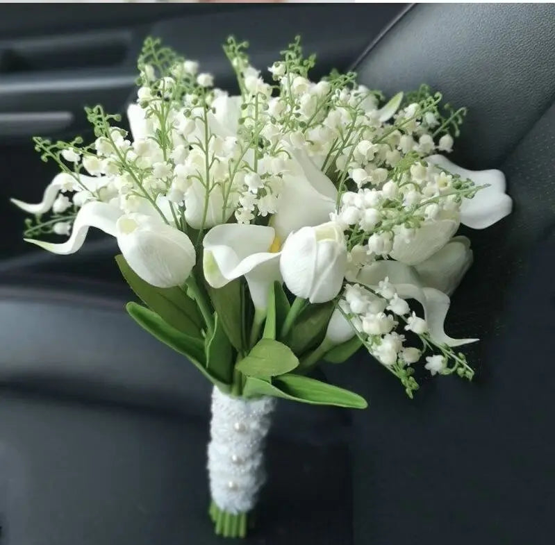 A handmade artificial wedding bouquet featuring a mix of white calla lilies and lily of the valley with a pearl-accented lace handle.