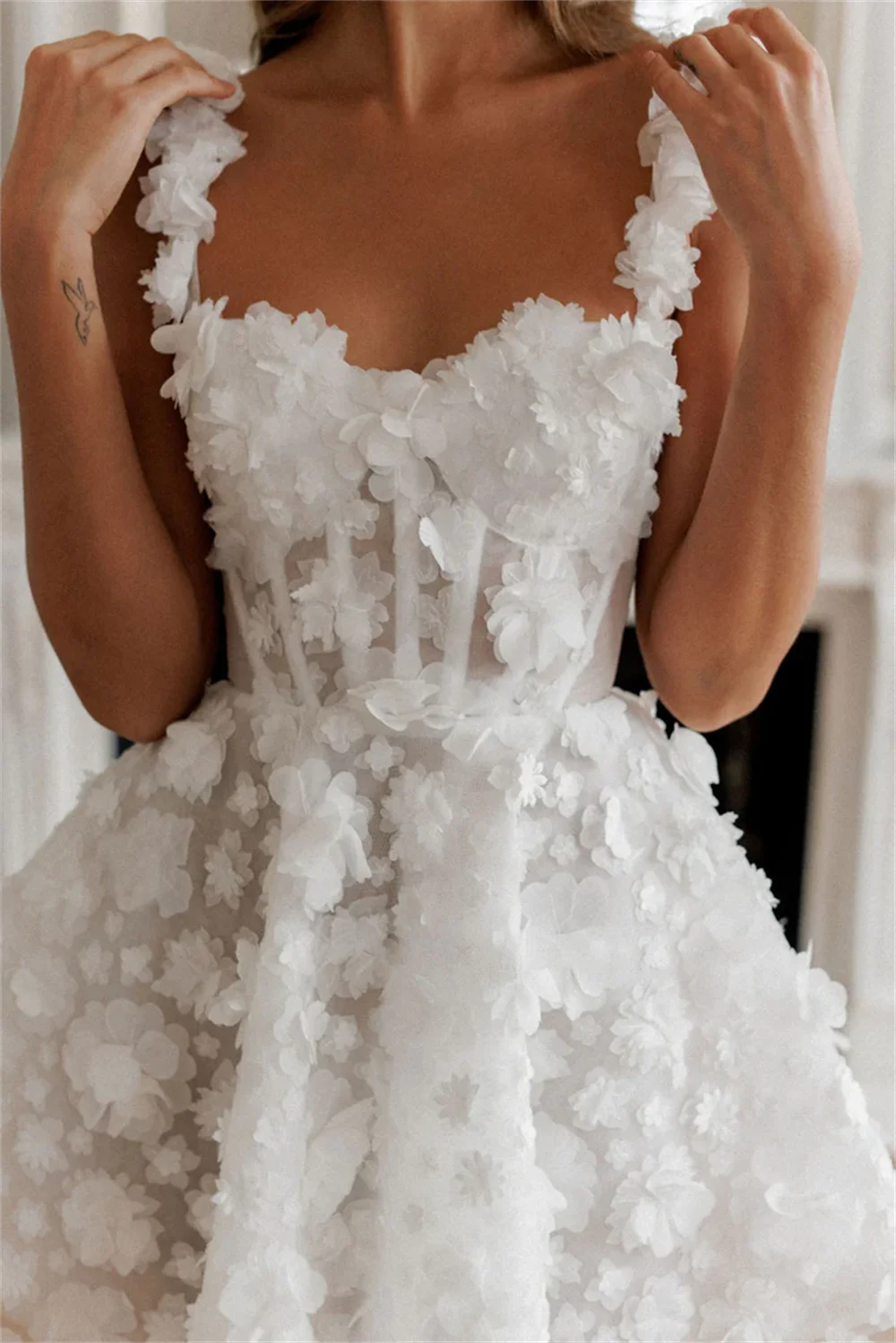 A detailed view of a white, strapless knee-length party dress bodice, featuring a corset-style structure and shimmering 3D flower lace appliqués.