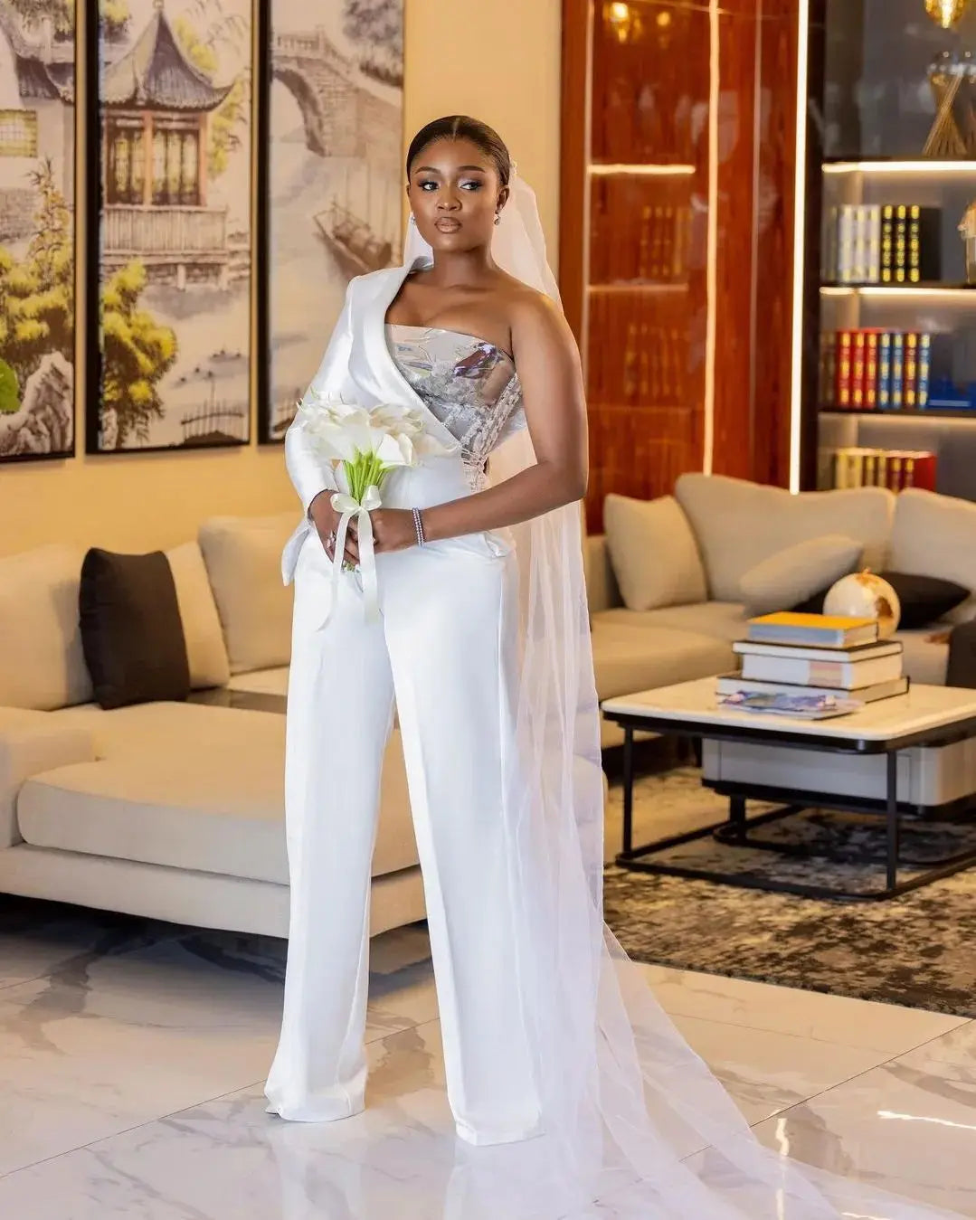 Full view of the elegant white asymmetric bridal jumpsuit gown, showcasing the clean lines of the high-waisted wide-leg pants paired with a sweeping cathedral-length wedding veil.