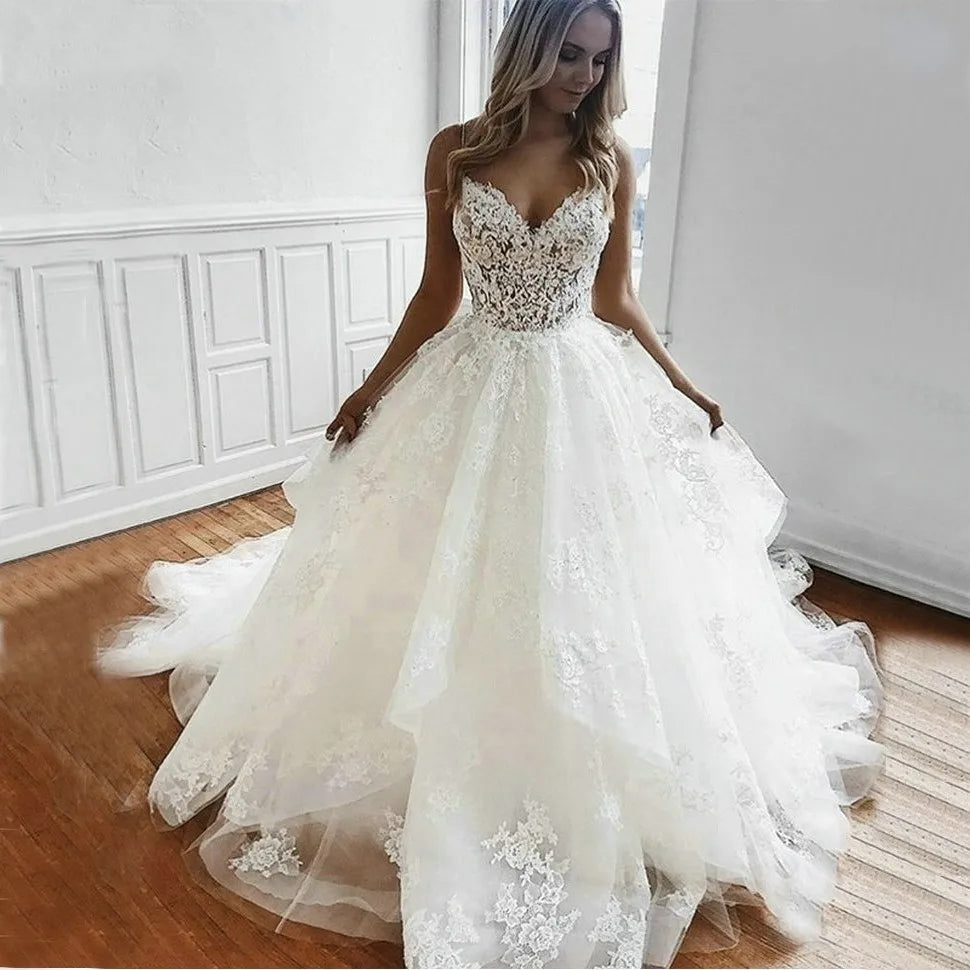 A bride posing in a white tulle A-line wedding dress with delicate lace appliqués and thin spaghetti straps.