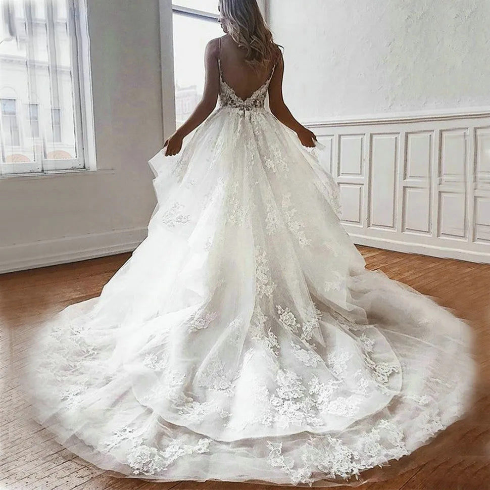 A full-length back view of a white tulle A-line bridal gown featuring intricate lace appliqué detailing and thin spaghetti straps.
