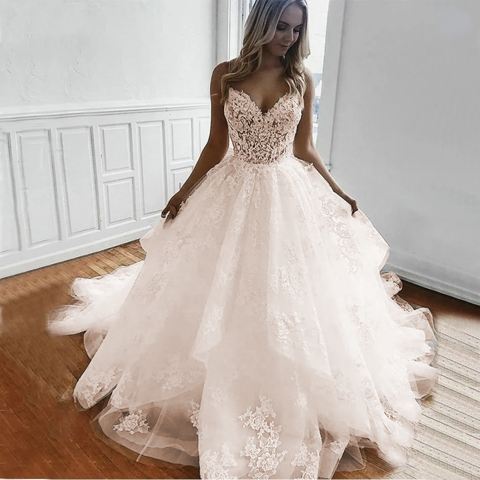 A beautiful bride showcasing a white tulle A-line wedding gown with floral lace appliqués and thin, delicate spaghetti straps.