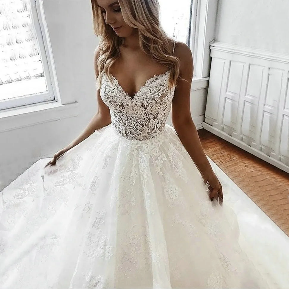 A close-up view of a bride posing in a white tulle A-line wedding dress, highlighting the intricate lace appliqué bodice and spaghetti straps.