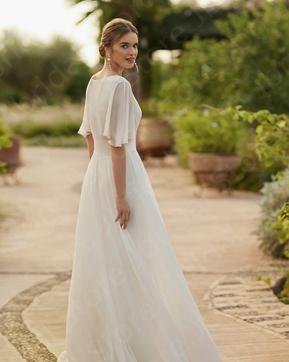 Rear three-quarter view of the bride showcasing the lightweight half-sleeve bridal top overlay and the sweeping, fluid silhouette of the bohemian wedding pantsuit.