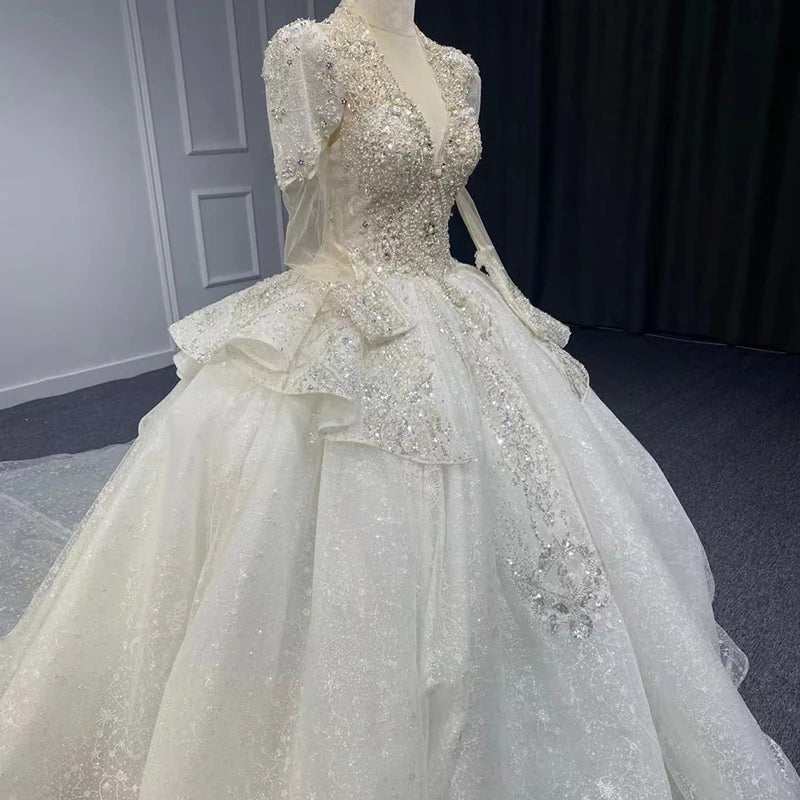 Detailed shot highlighting the sparkling novelty organza fabric texture, crystal beading, and floral appliqués on the long sleeve and shoulder of a bridal gown.