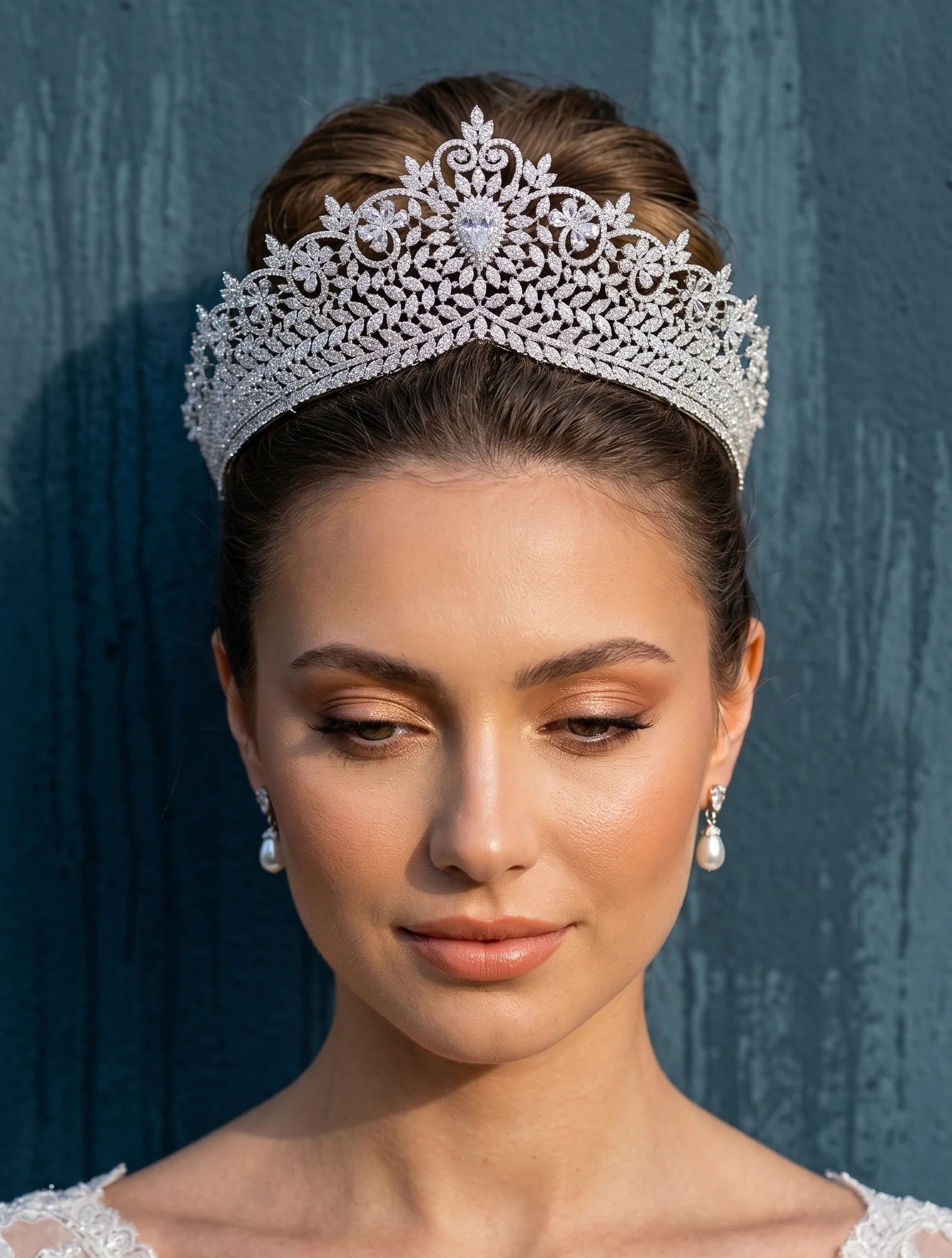 A bride with an elegant hair updo wearing a high-end zirconia wedding bridal crown tiara and matching pearl drop earrings.