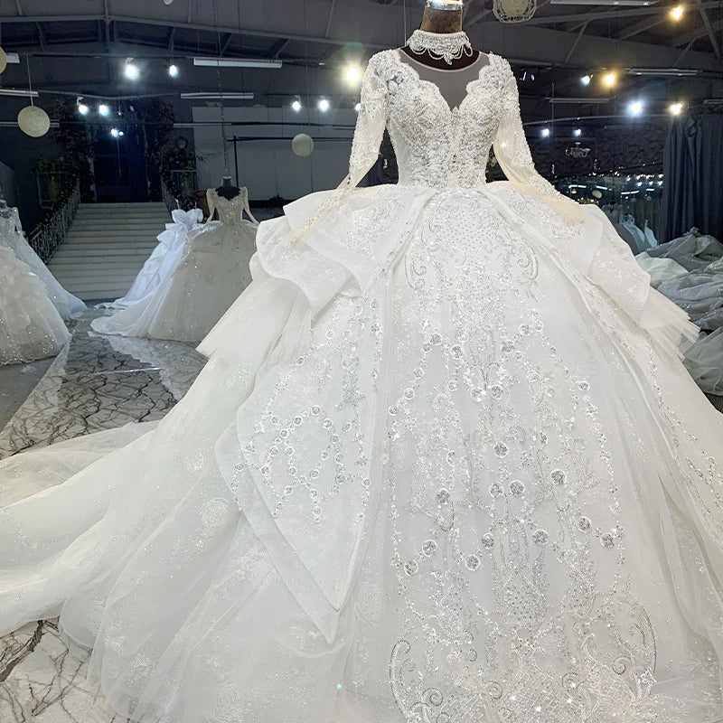 Side profile display of a structured long sleeve bridal ball gown, emphasizing the dramatic volume and fluid tiers of the ivory lace and tulle skirt.
