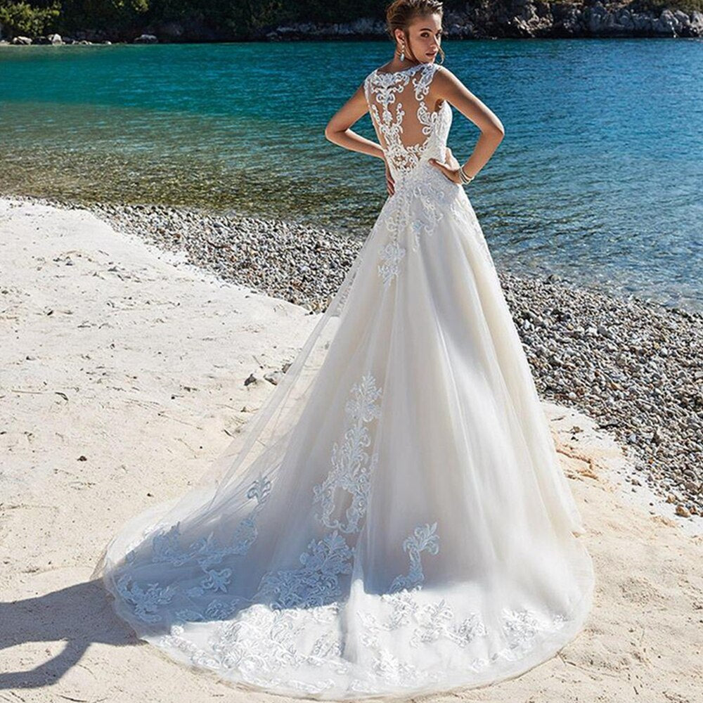 Full-length view of an elegant A-line bridal gown with intricate lace back detailing and a flowing skirt, set against a coastal backdrop.