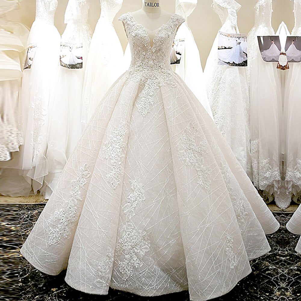 Mannequin display of a luxurious ball gown wedding dress with a V-neck, cap sleeves, and detailed lace appliques.