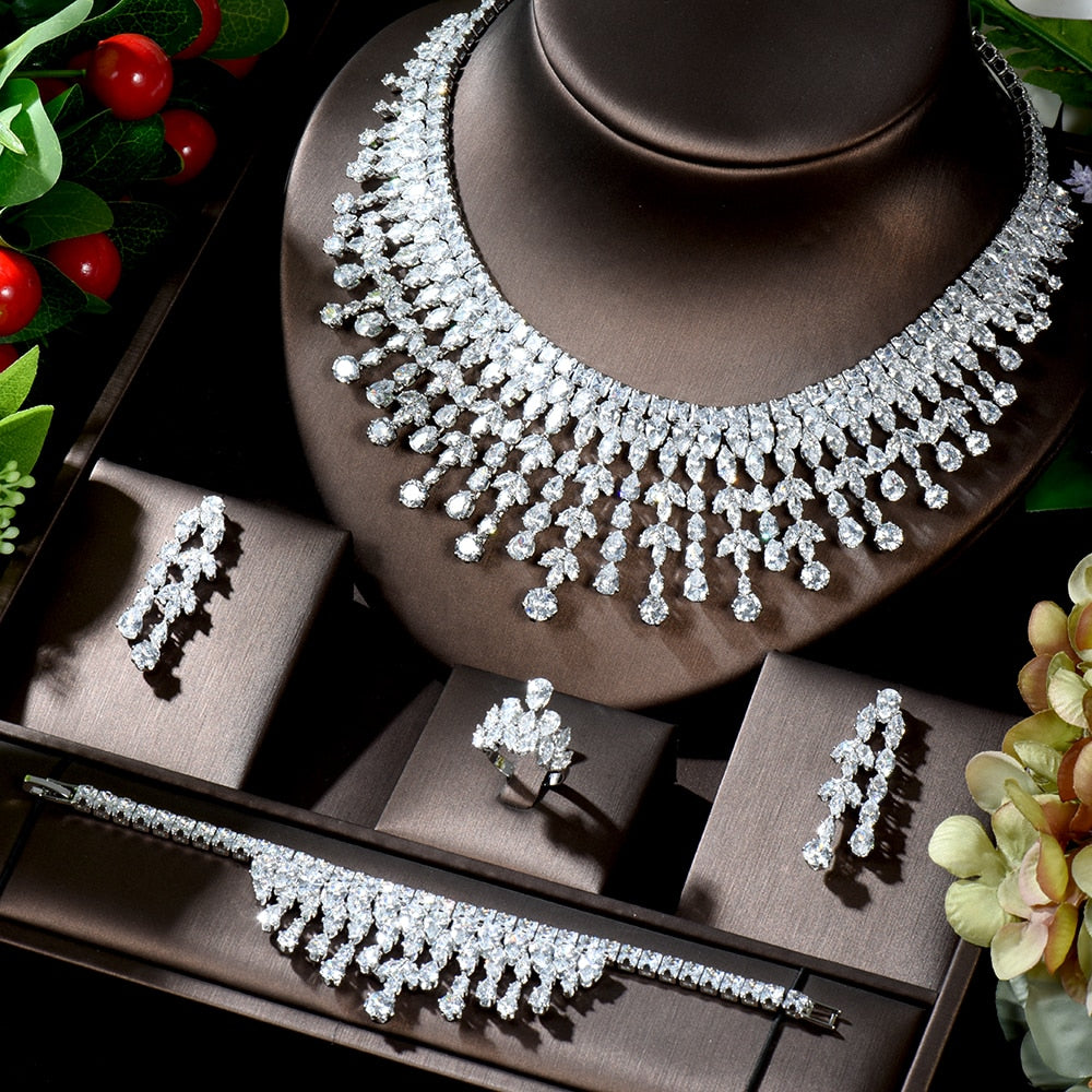 High-angle shot of a complete 4-piece elegant bridal wedding necklace set neatly arranged in a premium dark brown presentation box, showcasing the clear marquise-cut crystal collar necklace, matching drop earrings, statement ring, and fringe-style link bracelet alongside red berry accents.