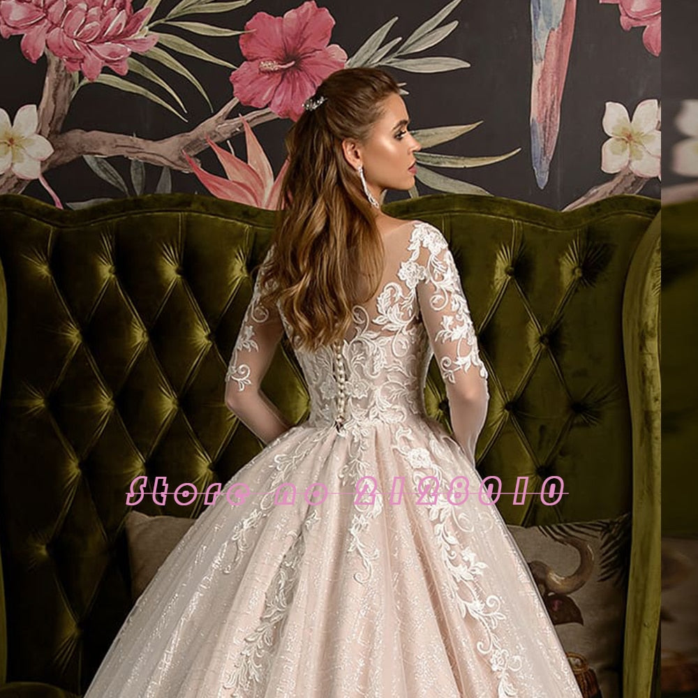 Back view of a bride wearing a shiny long-sleeve wedding gown, highlighting the detailed lace back and full ball gown skirt.