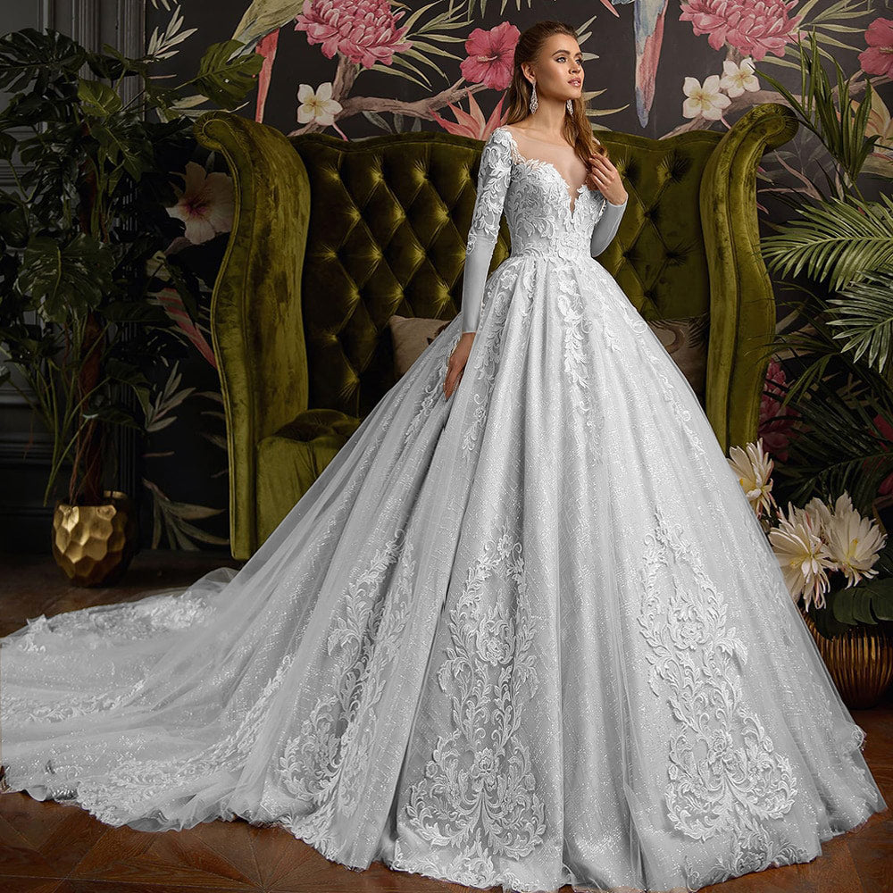 Front-facing portrait of the bride modeling a long-sleeve shiny ball gown with a deep V-neck and delicate lace detailing.
