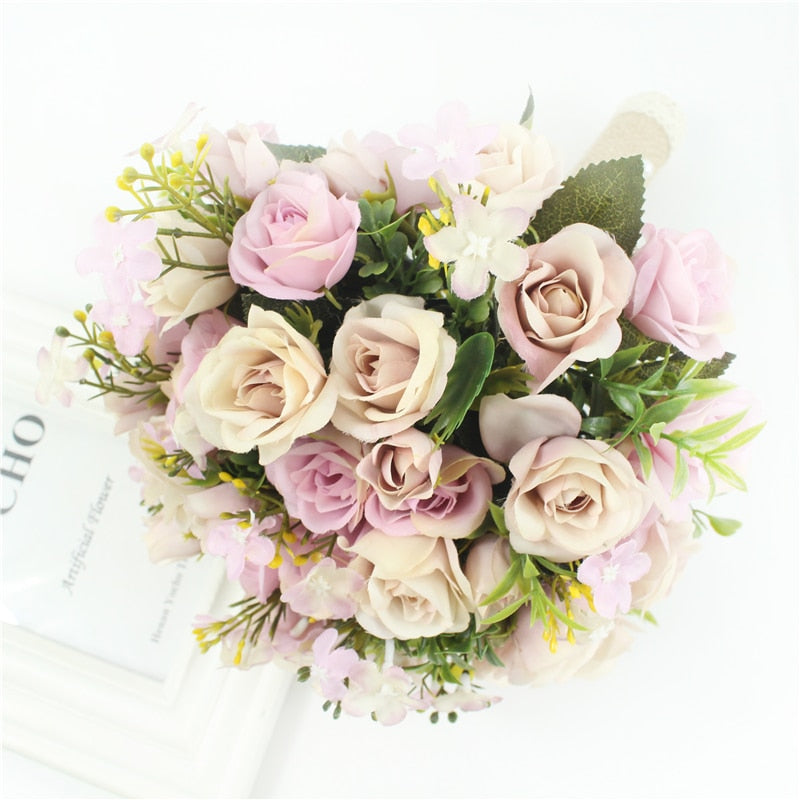 Overhead close-up shot of an elegant handmade wedding bouquet filled with realistic dusty pink, mauve, and champagne silk roses interspersed with green leaves and delicate filler blooms.
