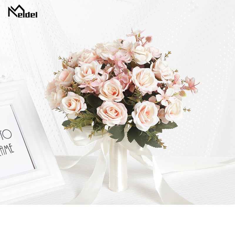 Front look at a romantic dusty pink artificial bridal bouquet composed of soft pink and ivory silk roses arranged with small matching ribbons on a texturized white fabric backdrop.