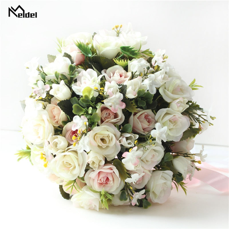 Close-up studio product shot of a round artificial bridesmaid bouquet densely packed with blush pink and cream-colored faux roses interspersed with dark green leaves.