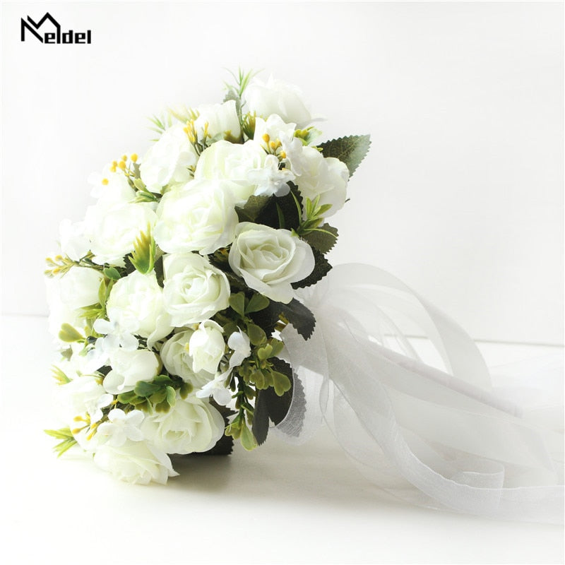Close-up side shot of a white faux rose bridal wedding bouquet featuring long trailing white satin ribbons cascading from a wrapped ivory handle.