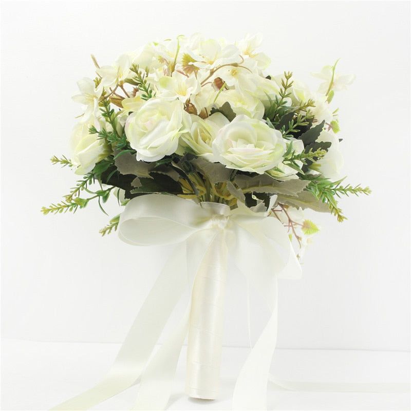 Elegant studio product shot of a minimalist cream-colored faux wedding bouquet featuring silk white roses, delicate green sprigs, and long flowing ivory satin ribbons.