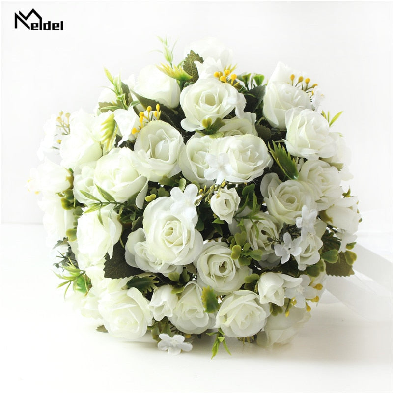 Top-down flat lay view of a faux bridal flower arrangement displaying closely packed white silk roses mixed with small green foliage and delicate yellow accent sprigs.