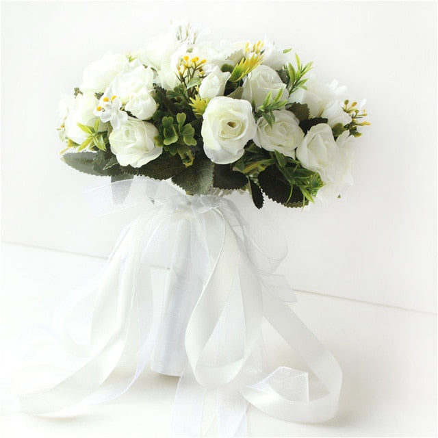 Low-angle view looking up at an all-white artificial bridal bouquet, showcasing the neatly tied green plastic stems bound together with wide, trailing white satin ribbons.
