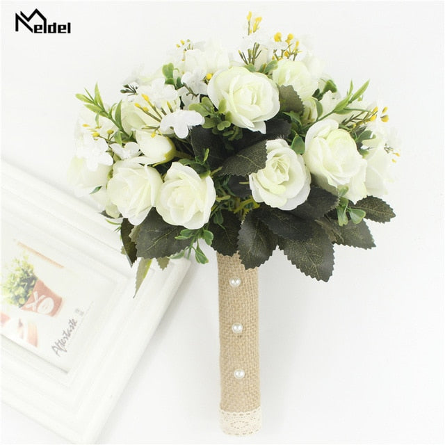 Front look at a round artificial flower wedding bouquet filled with creamy white silk roses, built with a decorative burlap handle accented by white pearls next to a white photo frame.