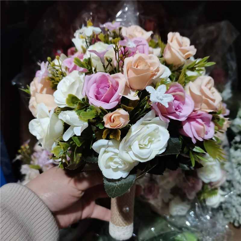 Detailed close-up photograph of a hand holding a flexible mixed faux rose wedding bouquet featuring tightly clustered silk roses in shades of lavender, peach, and cream.