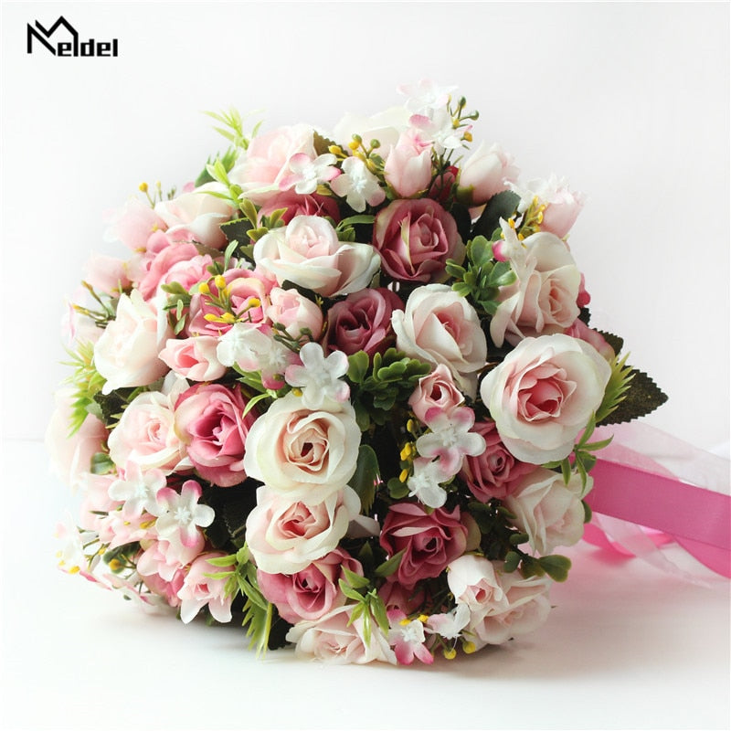 Overhead close-up shot of an elegant handmade wedding bouquet filled with realistic dusty pink, mauve, and champagne silk roses interspersed with green leaves and delicate white filler blossoms.