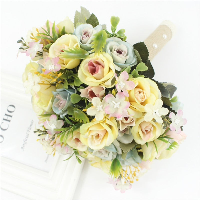 Overhead close-up shot of a multi-colored artificial wedding flower arrangement composed of pastel yellow, dusty blue, and soft pink silk roses.