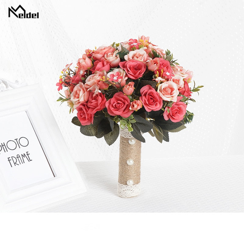 Brightly lit product display of a round artificial wedding bouquet showcasing coral, peach, and deep pink silk roses, built with a decorative burlap and lace stem wrap next to a white photo frame.