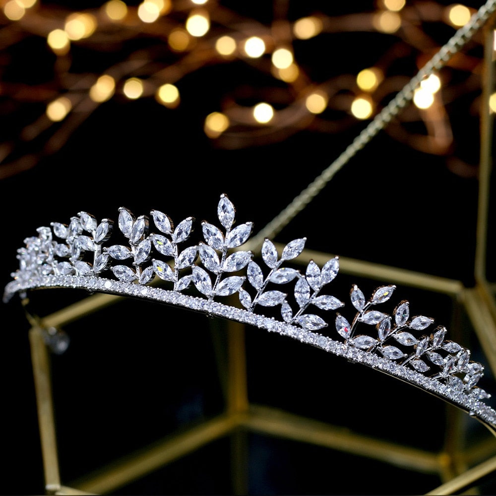 Close-up side perspective of a silver leaf bridal wedding tiara showing rows of shimmering marquise-cut crystal foliage sprigs against a soft bokeh background of golden fairy lights.