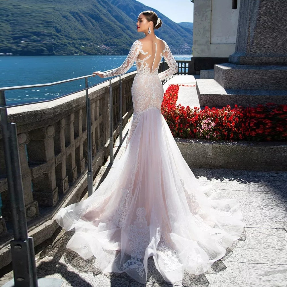 Rear full-length view of a bride wearing a luxury long-sleeve mermaid wedding dress, showcasing the flowing lace train and elegant illusion lace back design.