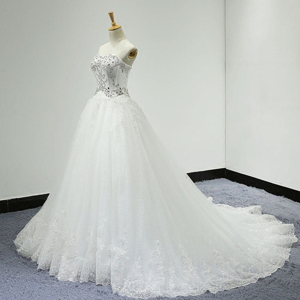 Side view of a bridal mannequin wearing a sparkly A-line wedding dress with an off-the-shoulder neckline, beaded corset bodice, and a full tulle skirt with lace trim.